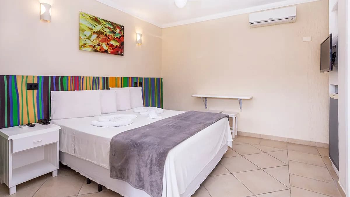 Suíte da Pousada Azul da Cor do Mar com cama de casal, cabeceira listrada colorida e ar-condicionado