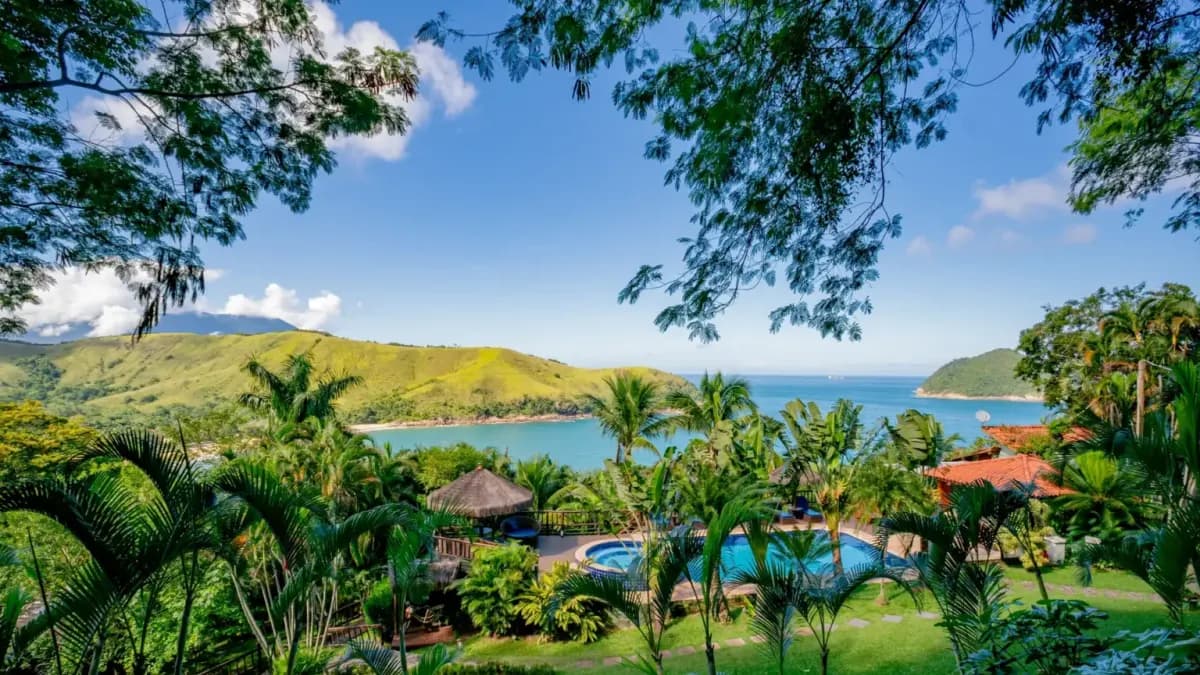 Vista do alto do Ilha de Toque Toque Eco Hotel, com jardim, coqueiros, piscina e a enseada de Toque Toque Grande entre morros verdes