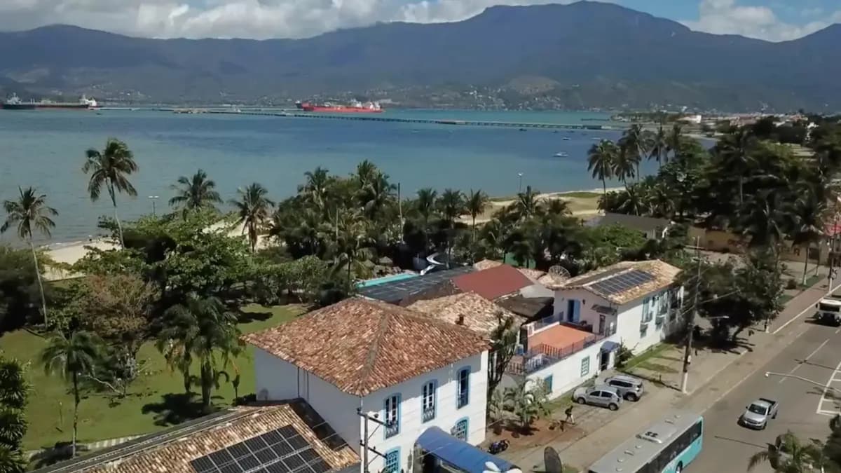 Vista aérea do Porto Grande Hotel, com telhados e jardins arborizados de frente para o canal de São Sebastião e a serra de Ilhabela