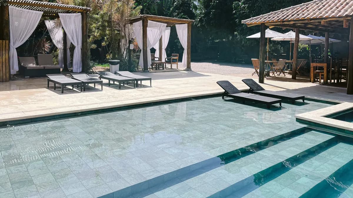 Piscina de azulejos claros da Pousada Porto Mare com espreguiçadeiras e tendas de tecido branco entre a mata, em Maresias