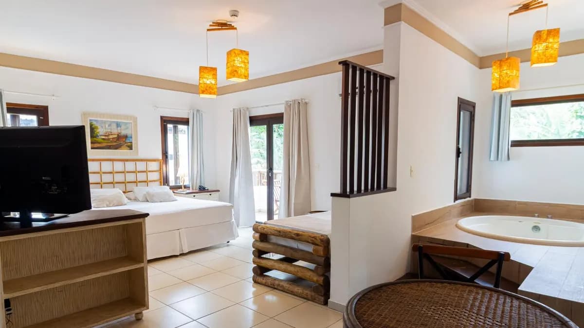 Suíte ampla da Pousada Porto Mare com cama de casal, banheira de hidromassagem e janelas para a mata