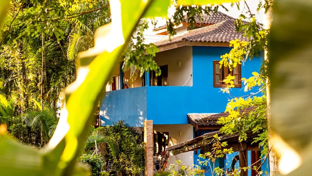 Prédio azul da Pousada Villa Blu com varandas de madeira entre plantas tropicais, em Maresias