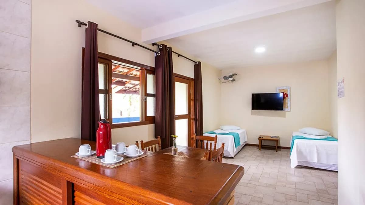 Flat da Pousada Villa Blu com balcão de madeira, mesa, duas camas de solteiro e televisão