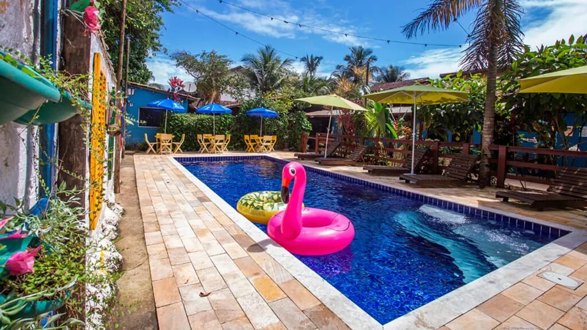 Piscina da Pousada Villa Blu com boia de flamingo rosa, guarda-sóis coloridos e coqueiros, em Maresias