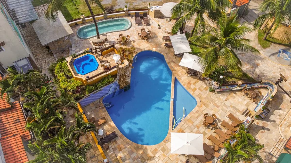 Vista aérea de la piscina azul en curva, con hidromasaje, reposeras y cocoteros, en el Villa'l Mare Hotel, en Maresias