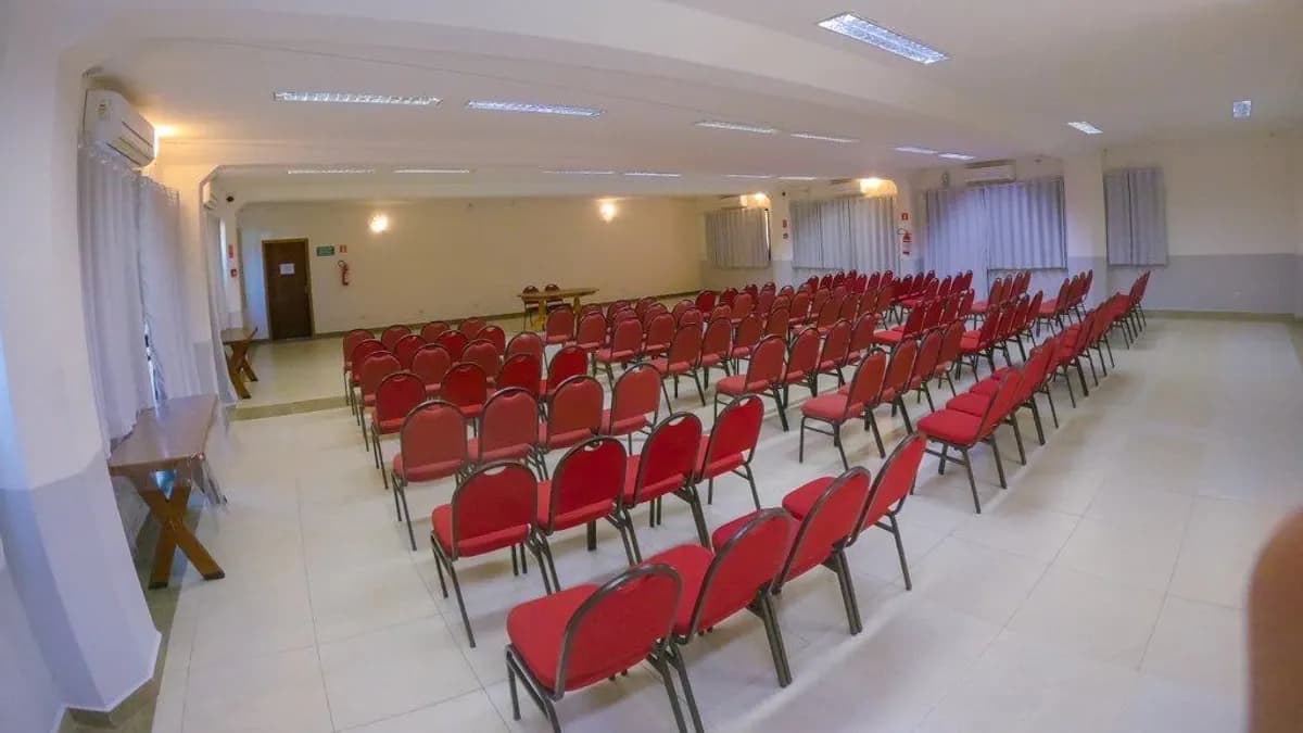 Salão de eventos do Villa'l Mare Hotel com fileiras de cadeiras vermelhas e janelas laterais