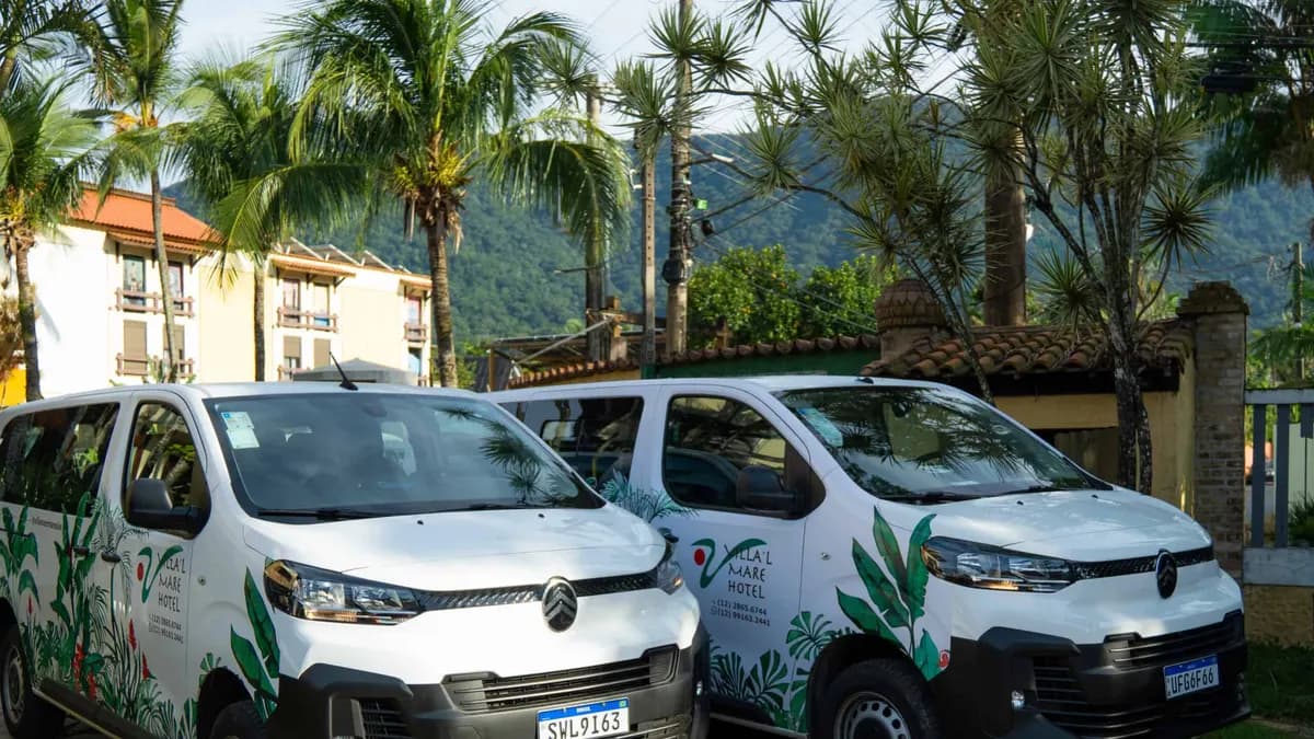 Duas vans brancas com a marca do Villa'l Mare Hotel estacionadas diante do hotel e da serra, em Maresias