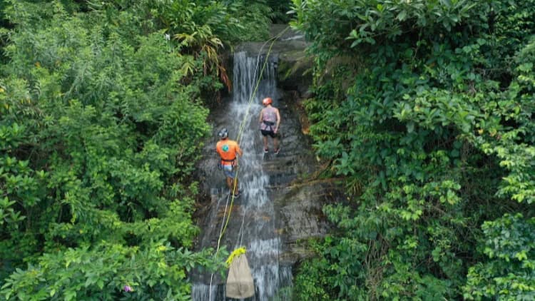 Vista aérea de dois praticantes de rapel descendo a queda-d'água estreita no meio da mata, na Cachoeira de Calhetas, em São Sebastião