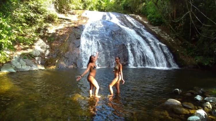Duas pessoas posam no poço raso diante da queda-d'água que desce pela rocha, na Cachoeira das 7 Quedas, em Maresias