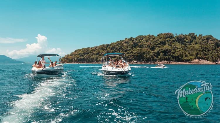 Duas lanchas com passageiros navegam em mar azul diante de ilha coberta de mata, no passeio pelas ilhas da Costa Sul de São Sebastião