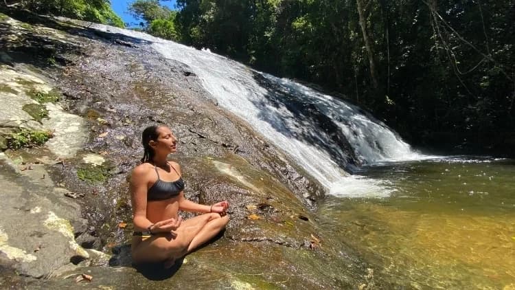 Visitante medita de pernas cruzadas sobre a rocha, ao lado da queda-d'água da Cachoeira das 7 Quedas, em Maresias