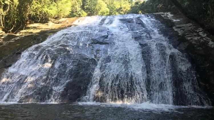 Água escorre em véus largos sobre a rocha escura até o poço da Cachoeira das 7 Quedas, em Maresias, com mata no alto